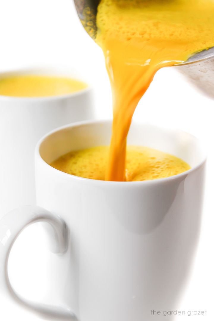 Vegan golden milk pouring into a white mug from the saucepan