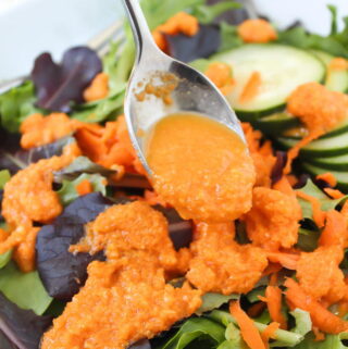 Close up of carrot ginger dressing being drizzled over lettuce with spoon