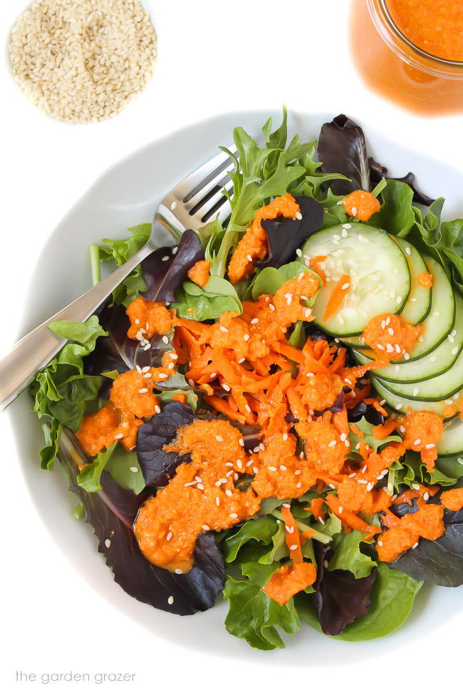 Green tossed salad in a bowl with carrot ginger dressing drizzled over top