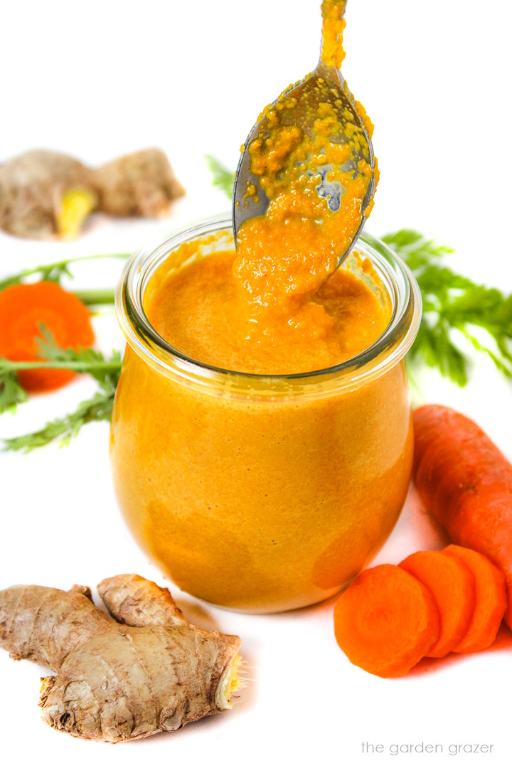 Spoon lifting up carrot ginger miso dressing out of a small glass jar