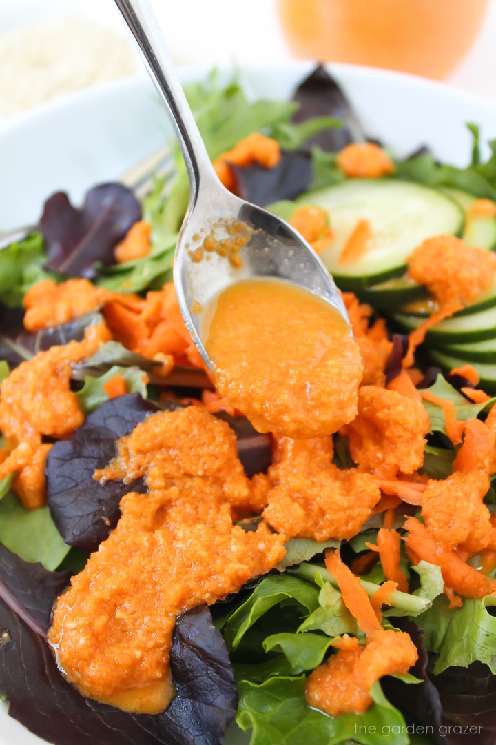 Spoon drizzling a Japanese-style carrot ginger miso dressing over a fresh greens salad