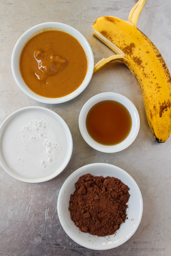 Ripe banana, soy milk, peanut butter, maple syrup, and cacao powder ingredients set out on a metal tray