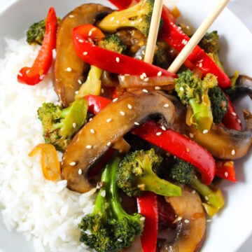 Portobello mushroom broccoli stir fry on a white serving plate with rice and chopsticks