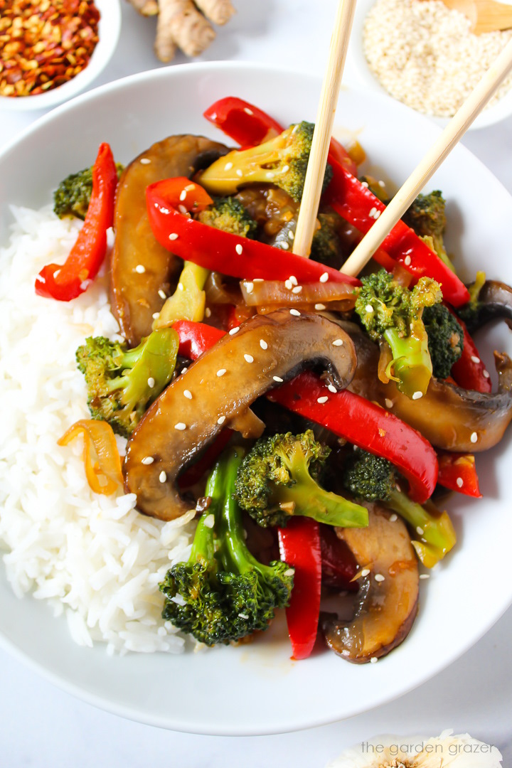 Portobello mushroom broccoli stir fry on a white serving plate with rice and chopsticks