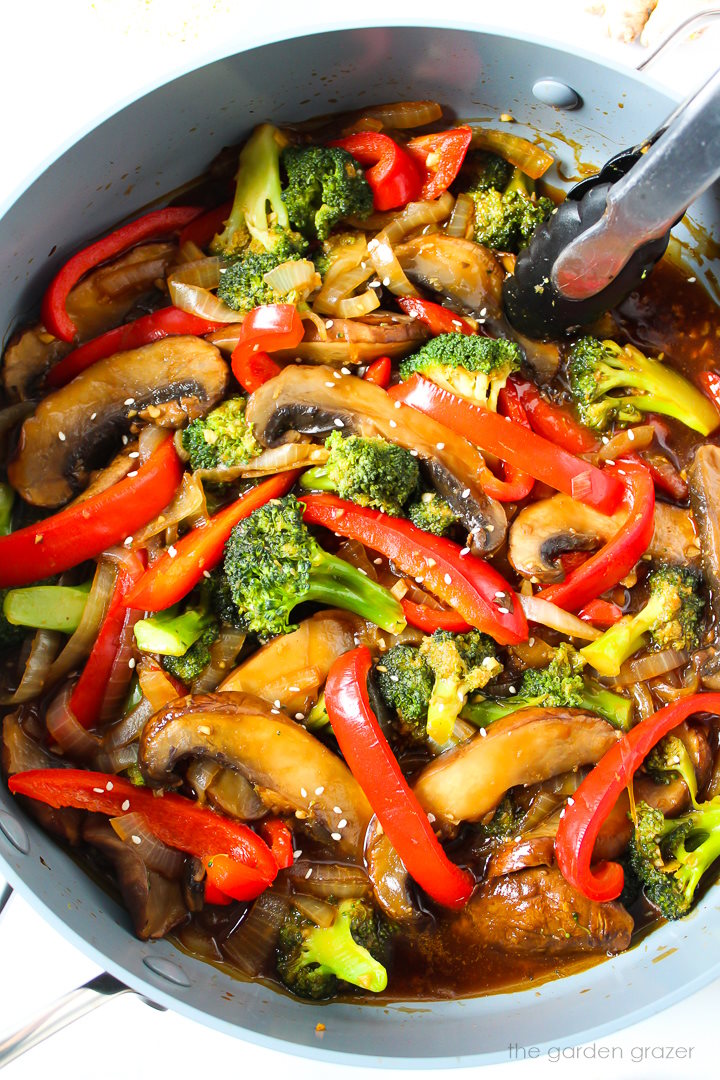 Portobello mushroom and broccoli stir-fry cooking in a large pan with tongs