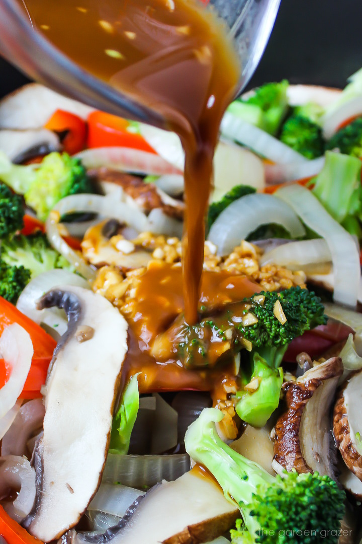 Pouring stir-fry sauce over broccoli and mushrooms in a cooking pan