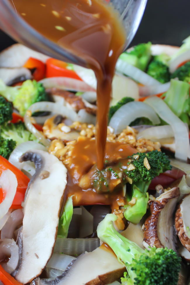 Asian-style sauce pouring over cooked vegetables in pan