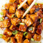 Chopsticks picking up teriyaki baked tofu from a white bowl