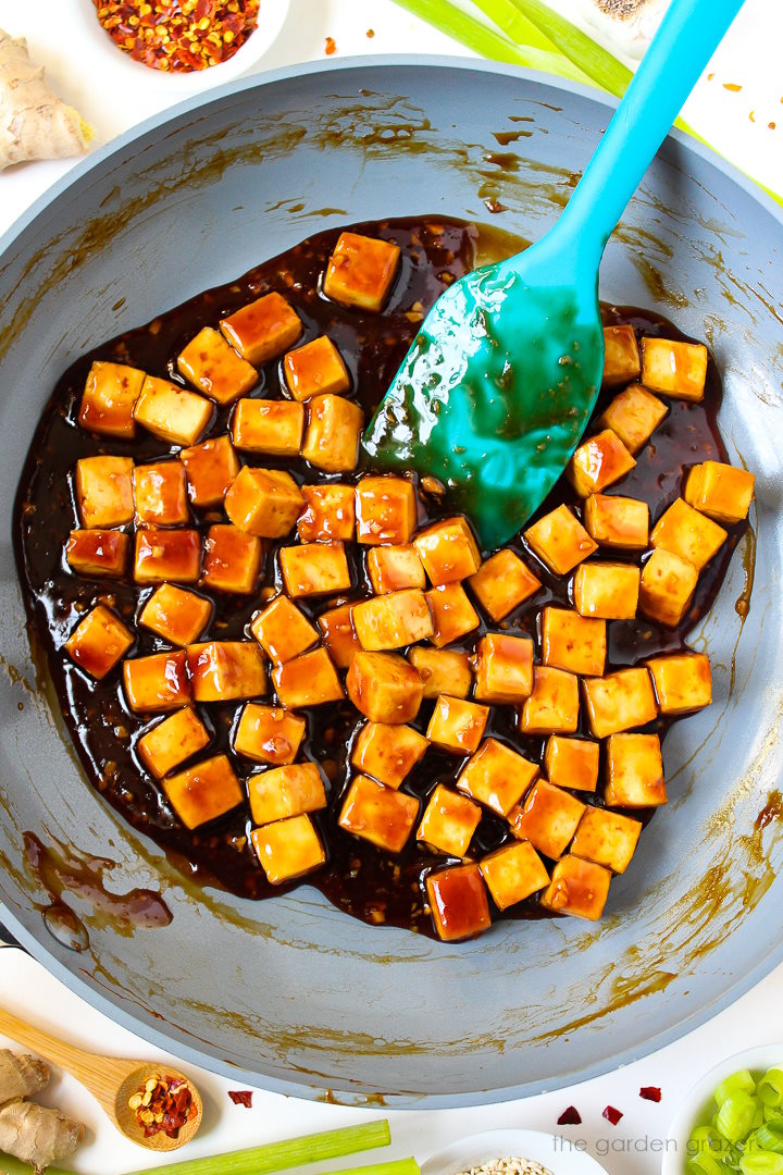 Overhead view of baked tofu cubes cooking in teriyaki sauce on a skillet