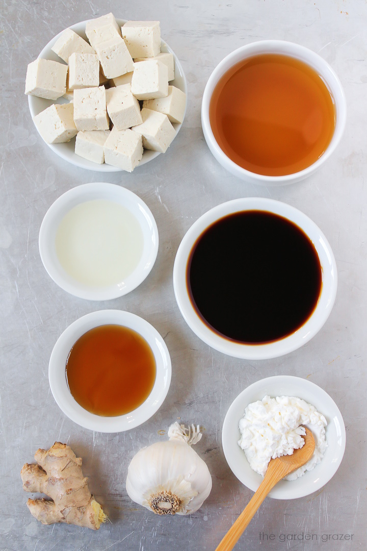 Vegetable broth, tamari, rice vinegar, maple syrup, garlic, and fresh ginger ingredients laid out on a metal tray
