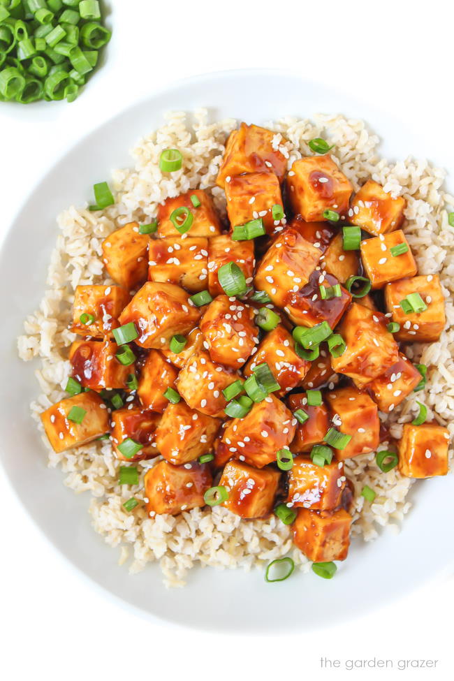 Tofu in a white bowl with cooked brown rice and homemade sauce