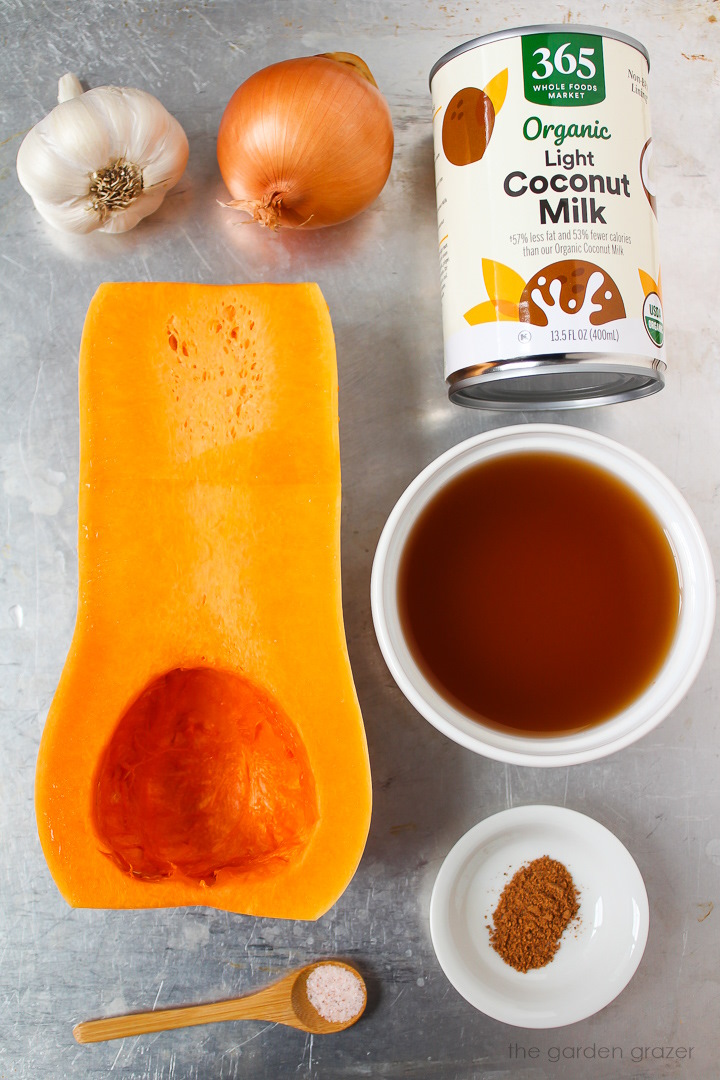 Squash, onion, garlic, canned coconut milk, vegetable broth, and spice ingredients laid out on a metal tray