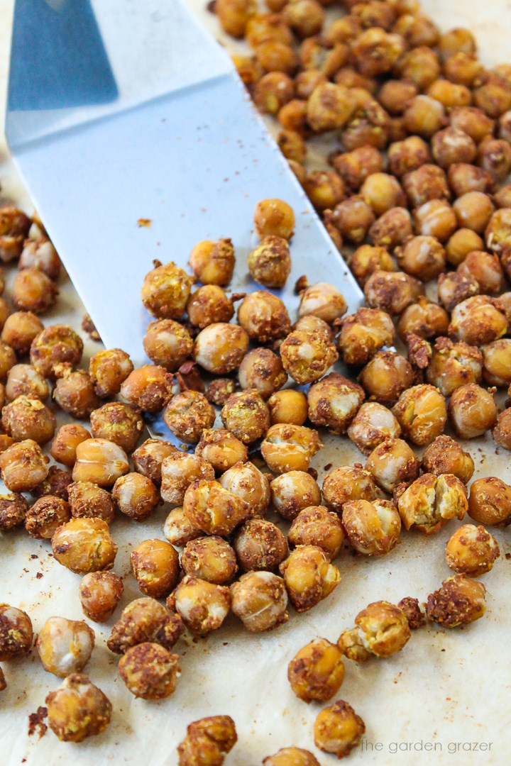 Metal spatula lifting up some cheesy nacho roasted chickpeas from a sheet pan