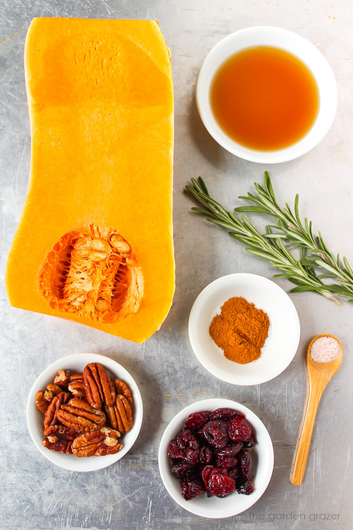 Butternut squash, maple syrup, fresh rosemary, pecans, cinnamon, and dried cranberry ingredients laid out on a metal tray