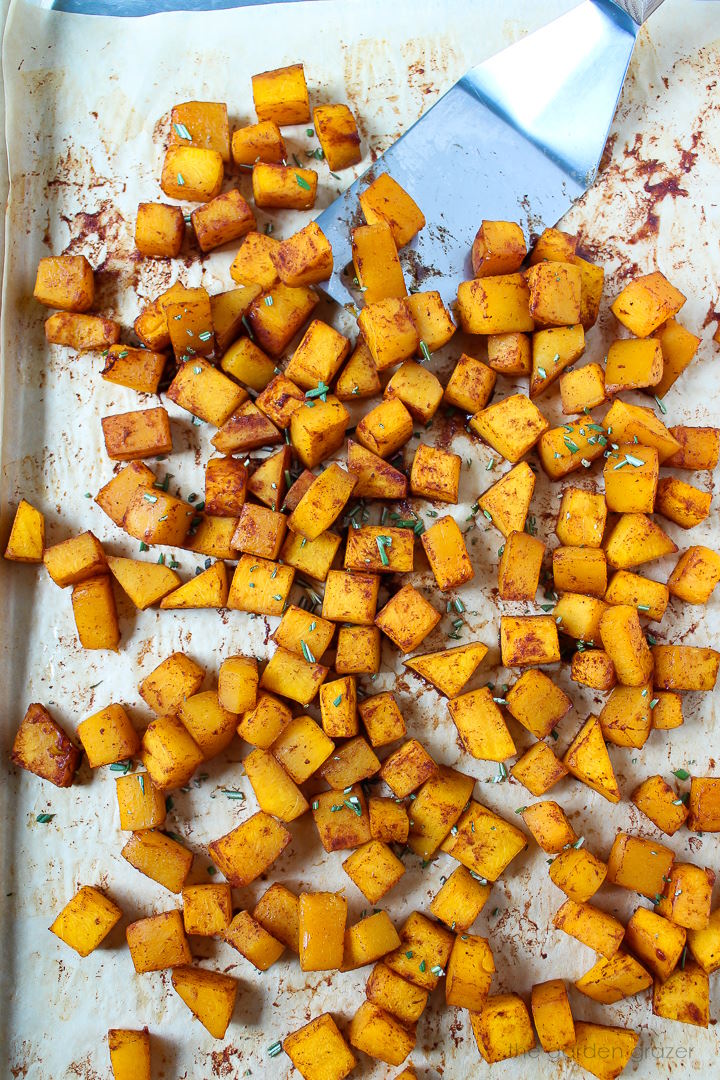 Overhead view of squash roasting on a sheet pan with metal spatula
