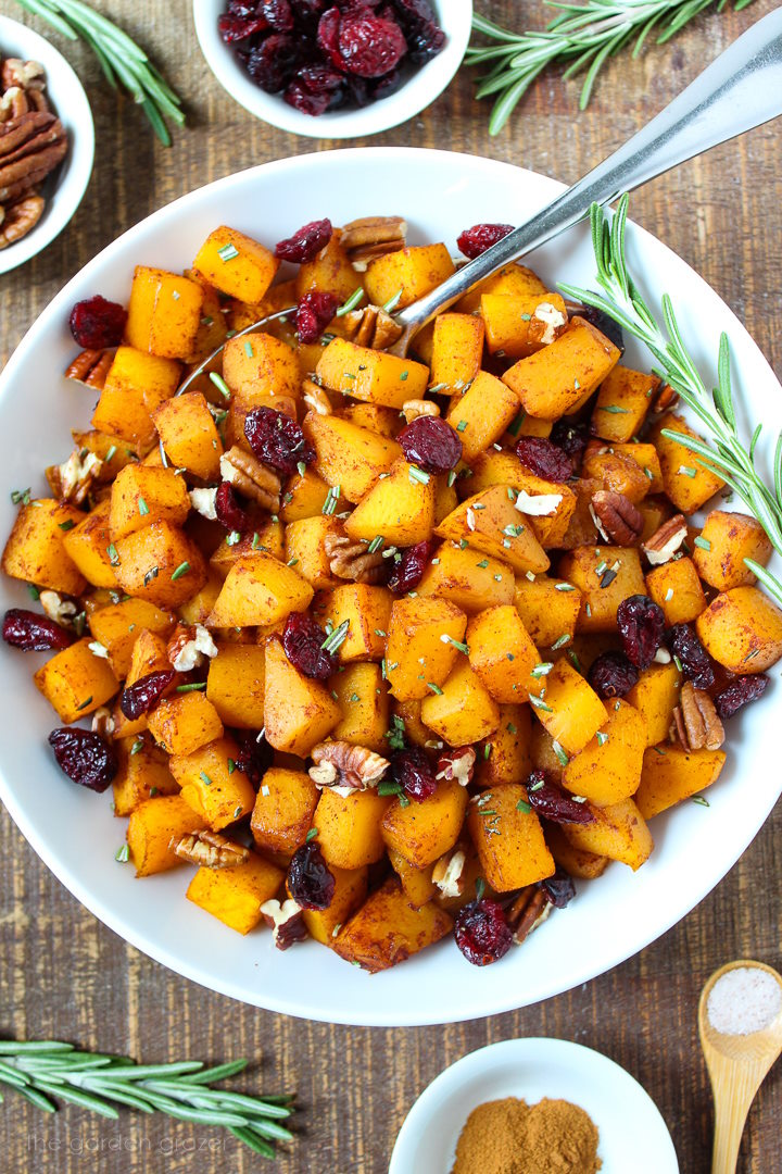 Maple cinnamon butternut squash garnished with fresh rosemary, pecans, and dried cranberries in a white serving bowl