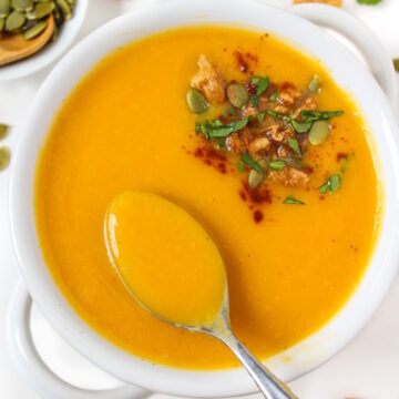 A spoon lifting up vegan butternut squash soup from a white serving bowl