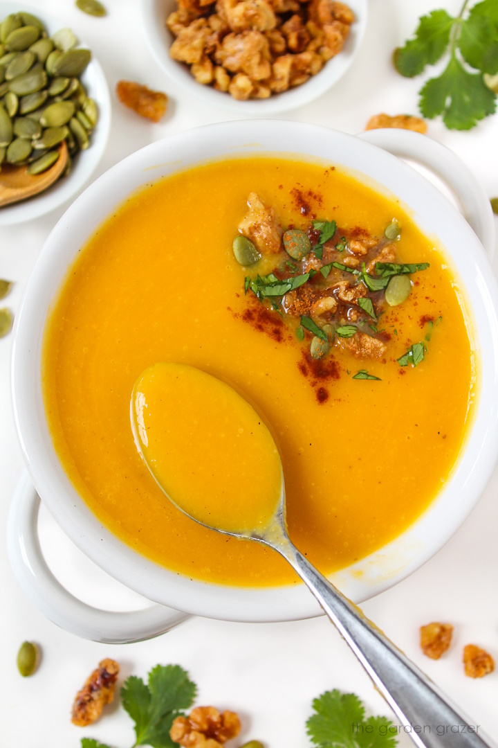 A spoon lifting up vegan butternut squash soup from a white serving bowl