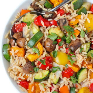 Bowl of roasted vegetable orzo tossed in garlic-balsamic dressing with spoon