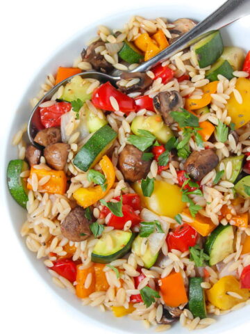 Bowl of roasted vegetable orzo tossed in garlic-balsamic dressing with spoon