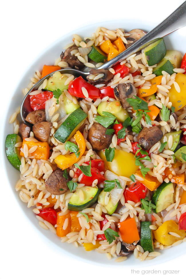 Bowl of roasted vegetable orzo tossed in garlic-balsamic dressing with spoon