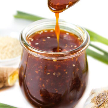 Spoon lifting up vegan teriyaki sauce from a small glass jar