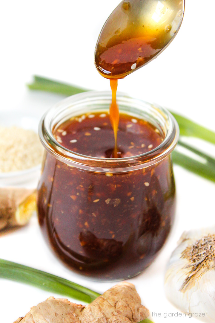 Spoon lifting up vegan teriyaki sauce from a small glass jar