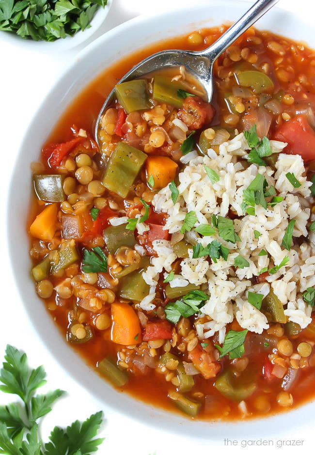 Bowl of bell pepper lentil soup topped with brown rice and parsley