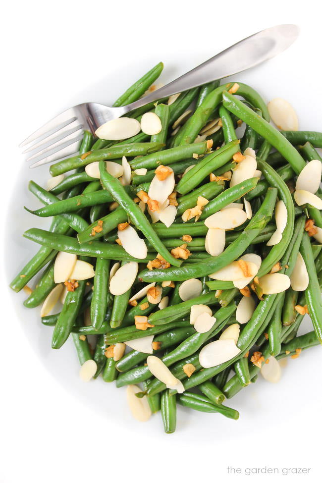 Garlic beans on a white plate sprinkled with sliced nuts