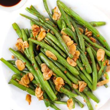 Cooked green beans with almonds, garlic, and tamari on a white plate with serving fork