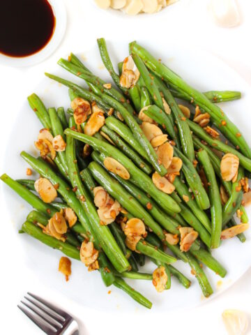 Cooked green beans with almonds, garlic, and tamari on a white plate with serving fork