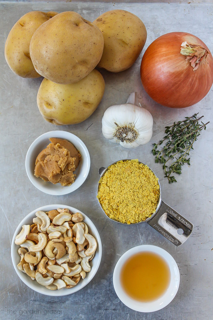 Gold potatoes, onion, garlic, cashews, miso, and nutritional yeast ingredients laid out on a metal tray