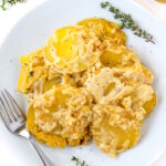 Vegan scalloped potatoes on a white plate with fork and fresh thyme