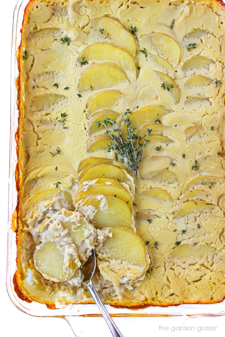 Overhead view of a spoon scooping into a pan of vegan scalloped potatoes