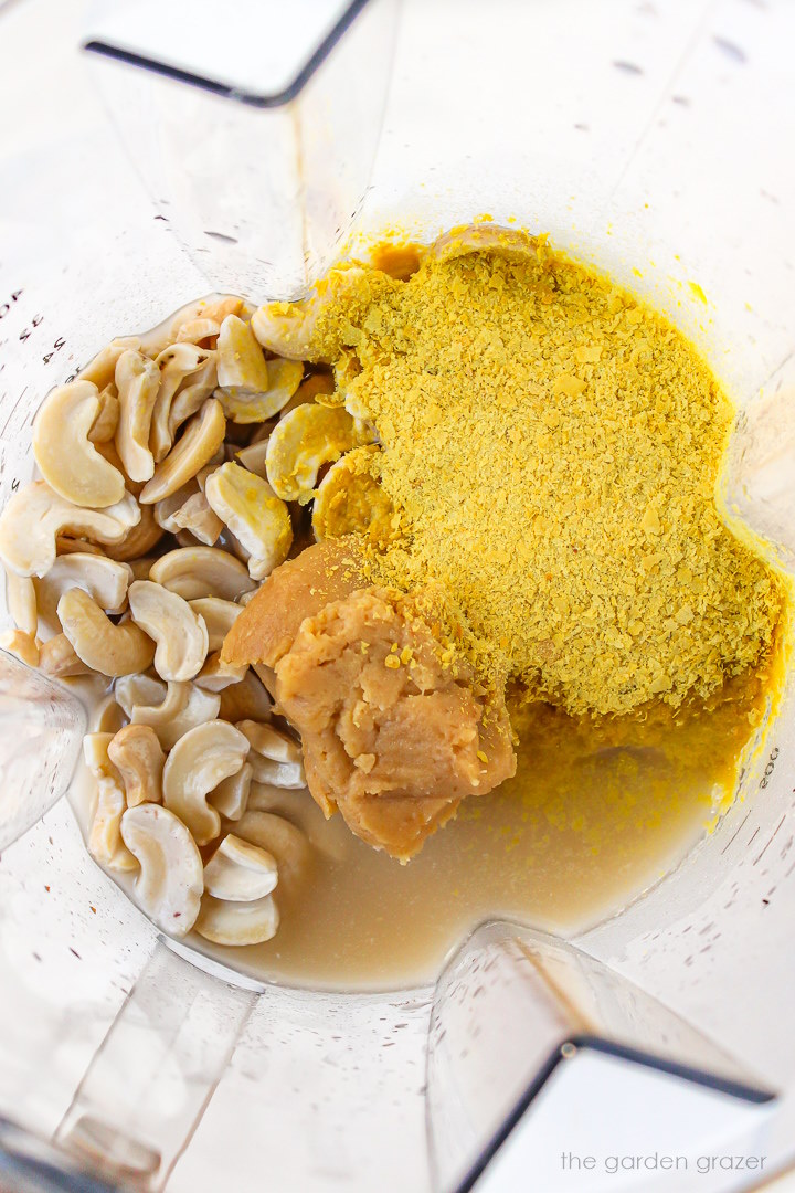 Overhead view of cheesy cashew sauce ingredients in a blender before blending