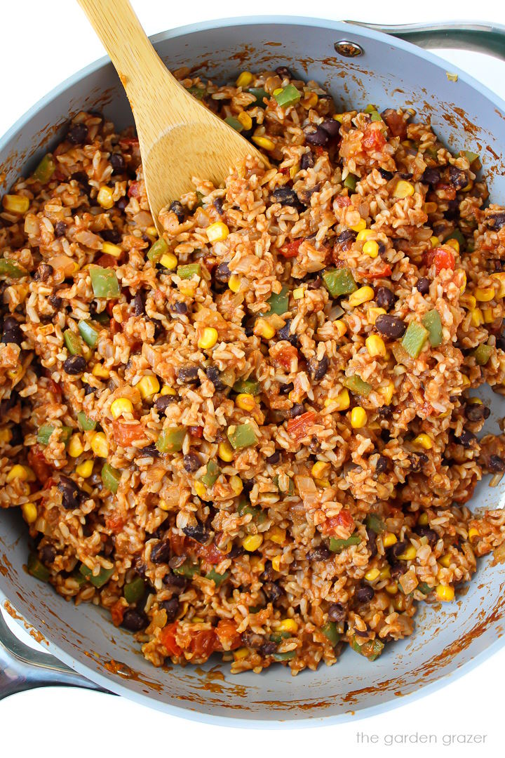 Overhead view of fiesta rice and black beans cooking in a large skillet with a wooden spoon