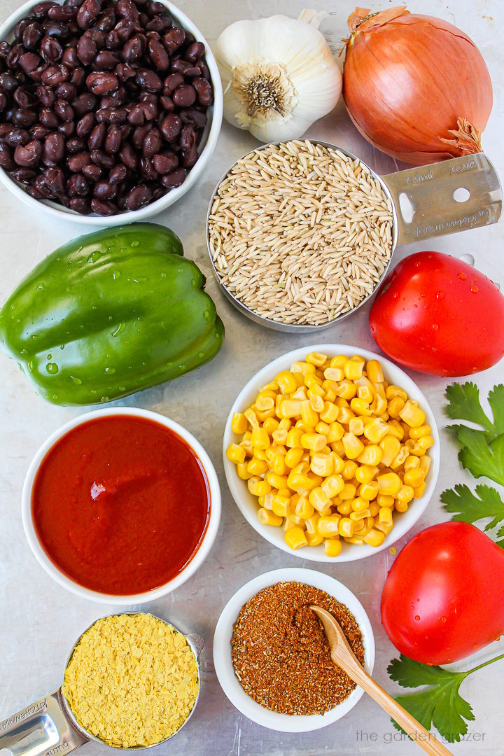 Onion, beans, bell pepper, garlic, tomato sauce, sweet corn, tomatoes, and taco seasoning ingredients laid out on a metal tray