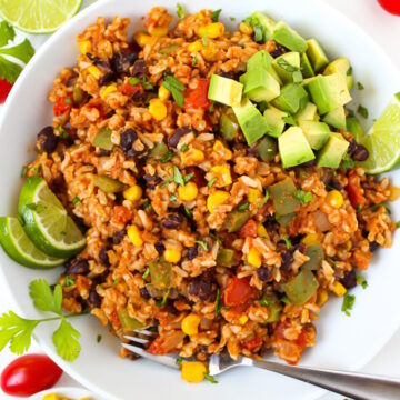 Overhead view of fiesta black beans and rice in a white bowl topped with avocado and lime slices