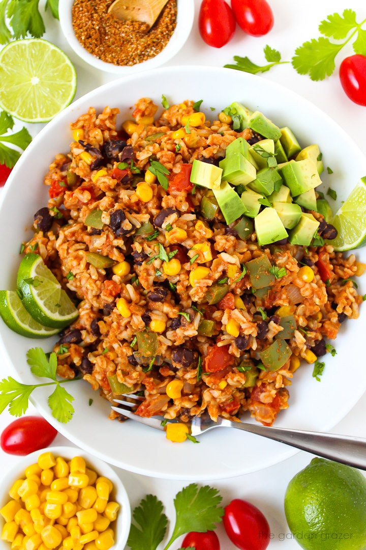 Overhead view of fiesta black beans and rice in a white bowl topped with avocado and lime slices