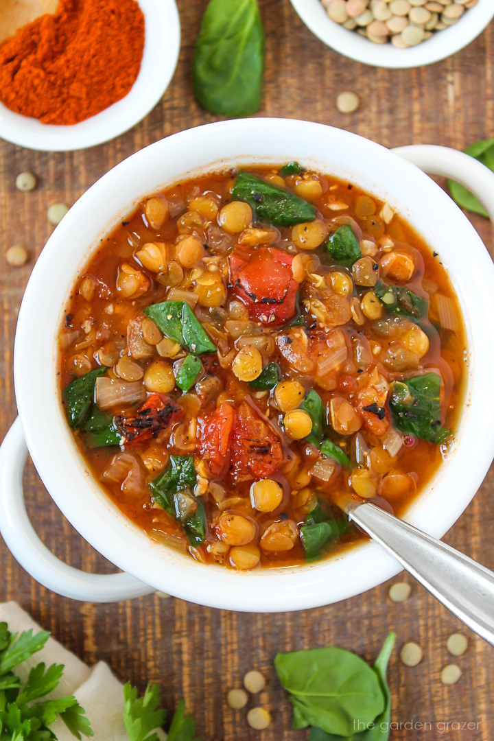 Smoky tomato lentil soup with spinach in a white bowl with serving spoon