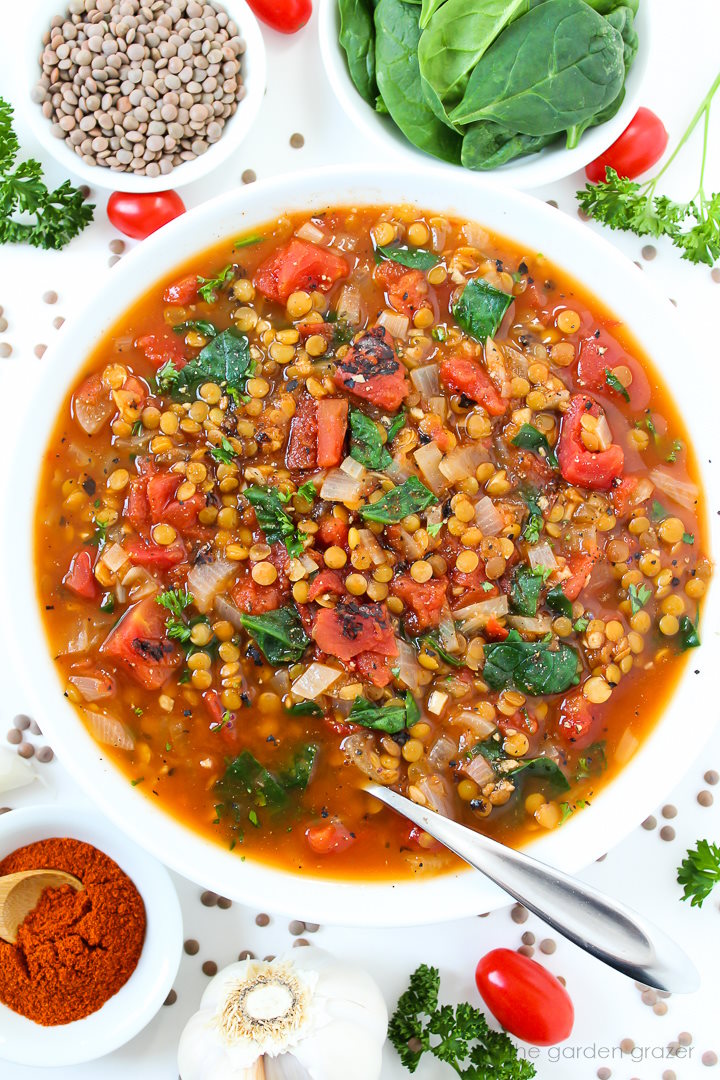 Smoky tomato lentil soup with spinach in a white bowl with serving spoon