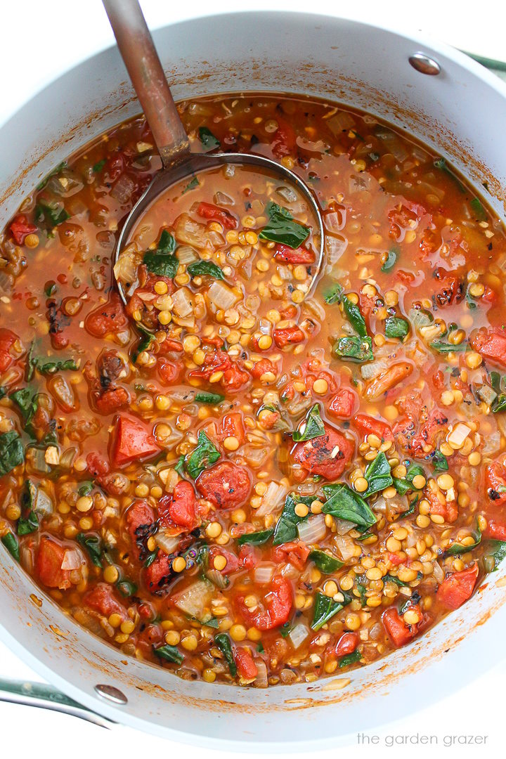 Smoky tomato lentil soup cooking in a large pot with ladle