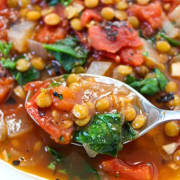 Close-up view of a spoon scooping up smoky tomato lentil soup with spinach from a white bowl