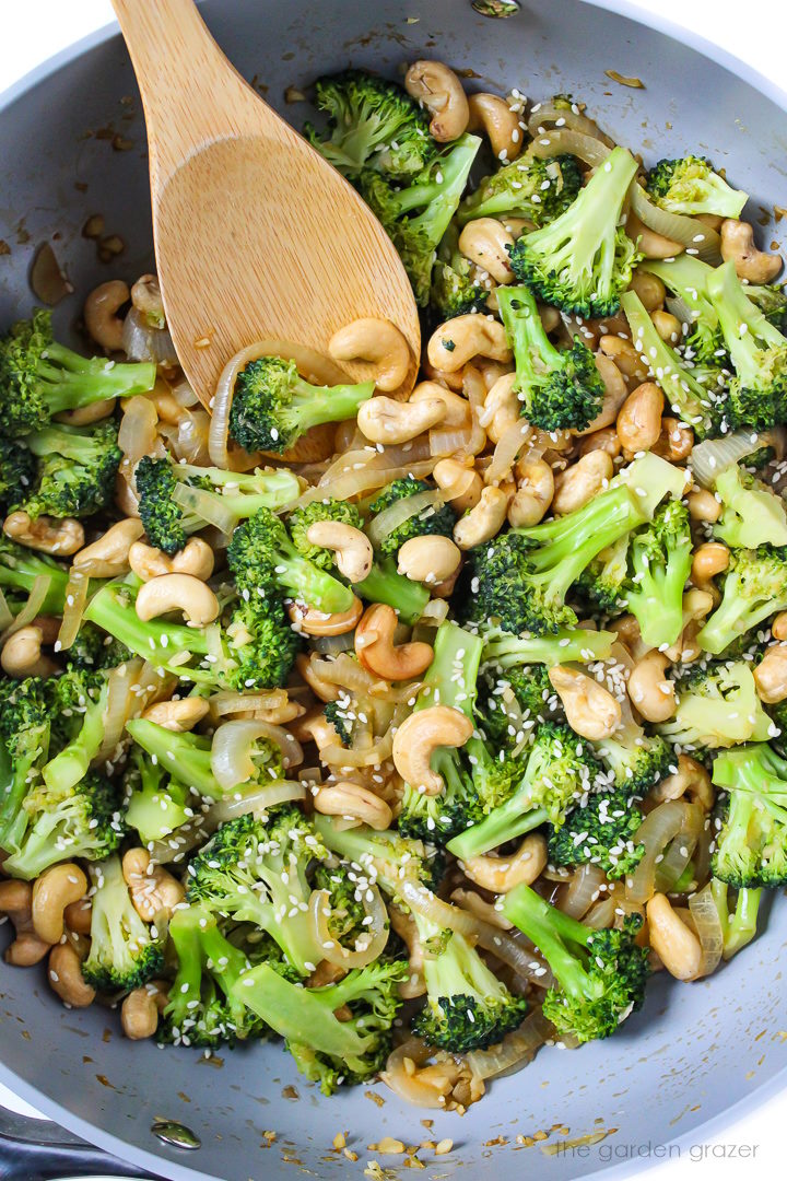 Overhead view of broccoli stir-fry cooking in a large pan with wooden stirring spoon