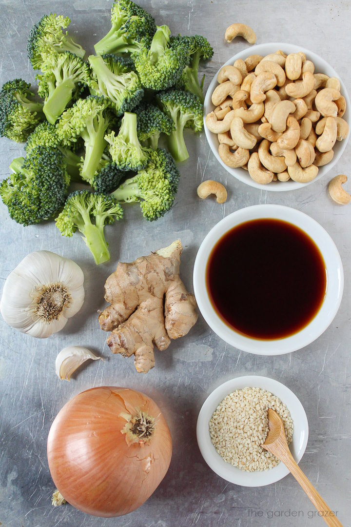 Roasted cashews, fresh broccoli, garlic, ginger, onion, and tamari ingredients laid out on a metal tray