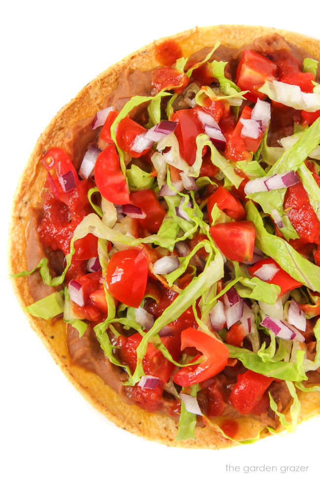 Vegan tostada with refried beans, tomato, lettuce, and onion