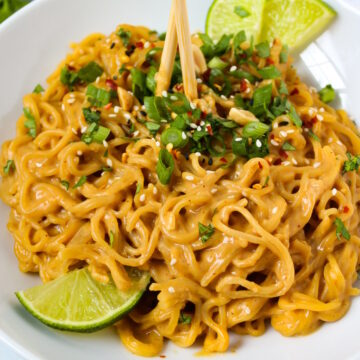 Vegan peanut noodles in a white serving bowl with lime slices and chopsticks