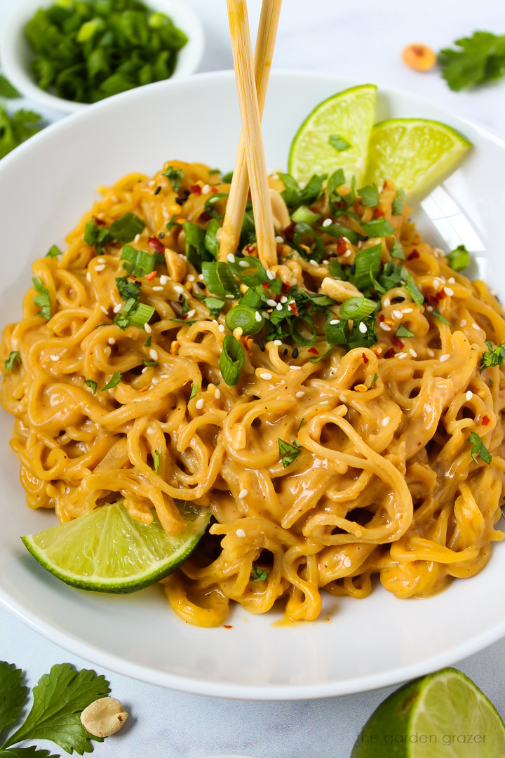 Vegan peanut noodles in a white serving bowl with lime slices and chopsticks