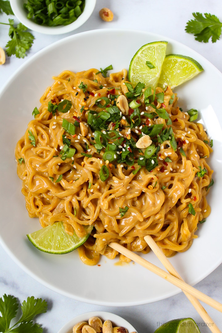 Overhead view of easy vegan peanut noodles served in a white bowl with fresh cilantro, lime slices, and green onions