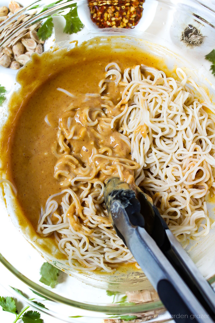 Overhead view of ramen noodles being mixed with a creamy peanut sauce in a glass bowl